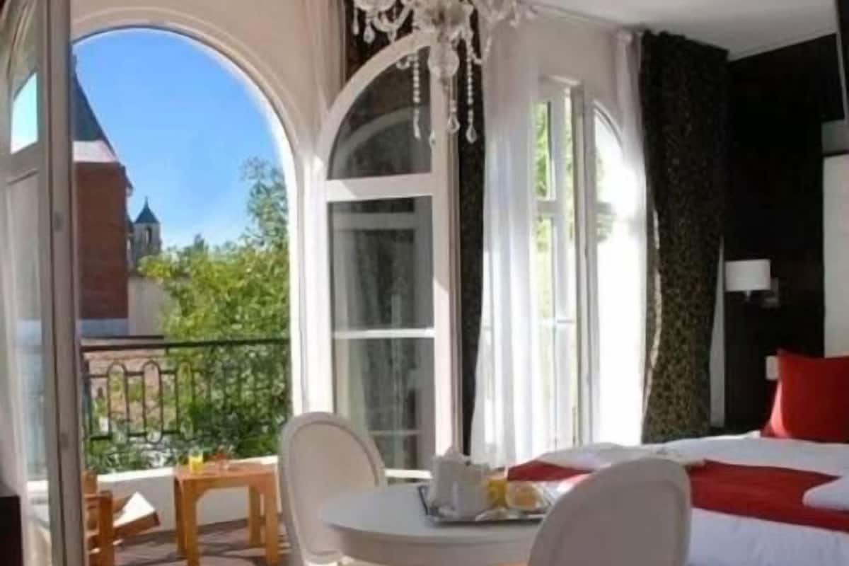 Une chambre à coucher comprenant un lit, une table, deux chaises et un balcon avec vue sur un immeuble et des espaces verts.