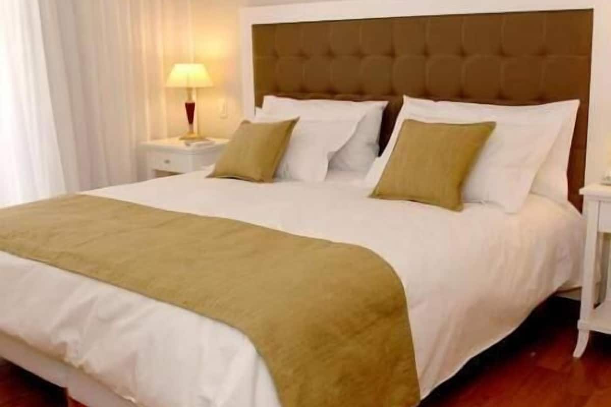 Une chambre d’hôtel avec un grand lit, du linge de lit blanc, une tête de lit marron et un plancher en bois.