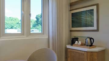 A room with a wicker chair, a small table, a cabinet with a coffee maker, and a framed picture on the wall.