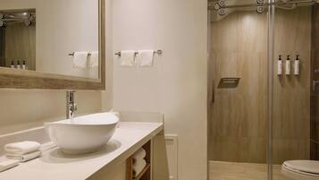 A modern bathroom with a large white sink, a glass shower enclosure, and a toilet.
