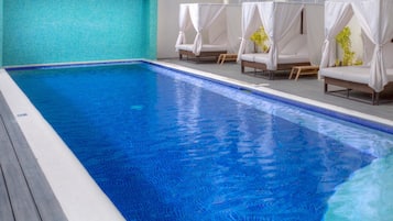 Una piscina con agua cristalina y azul, rodeada de sillas de descanso con toldos blancos.