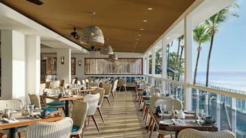 Un restaurante con mobiliario de mimbre, piso a rayas y vista al océano.