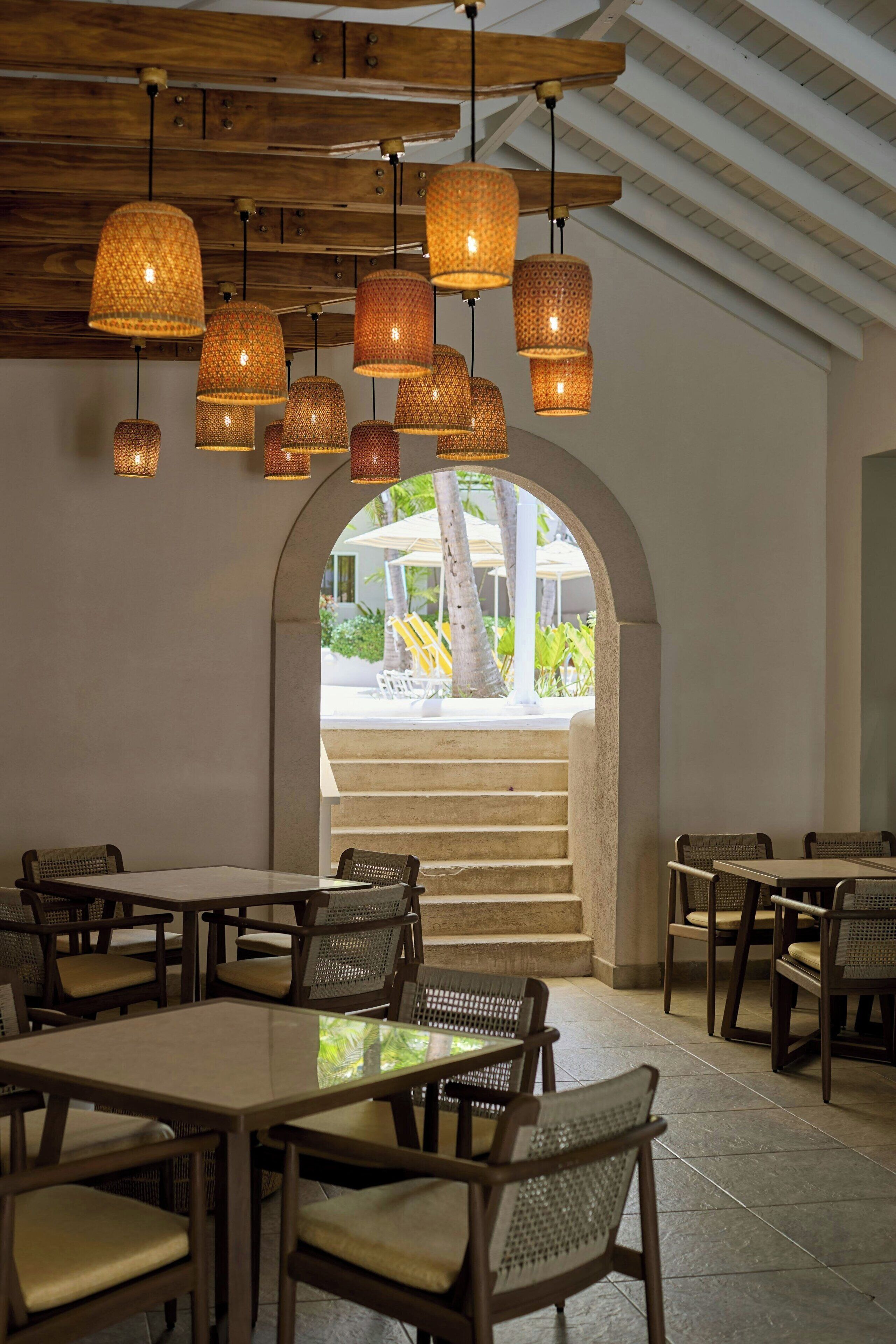 Un restaurante con varias mesas y sillas, techo de madera y luces colgantes.