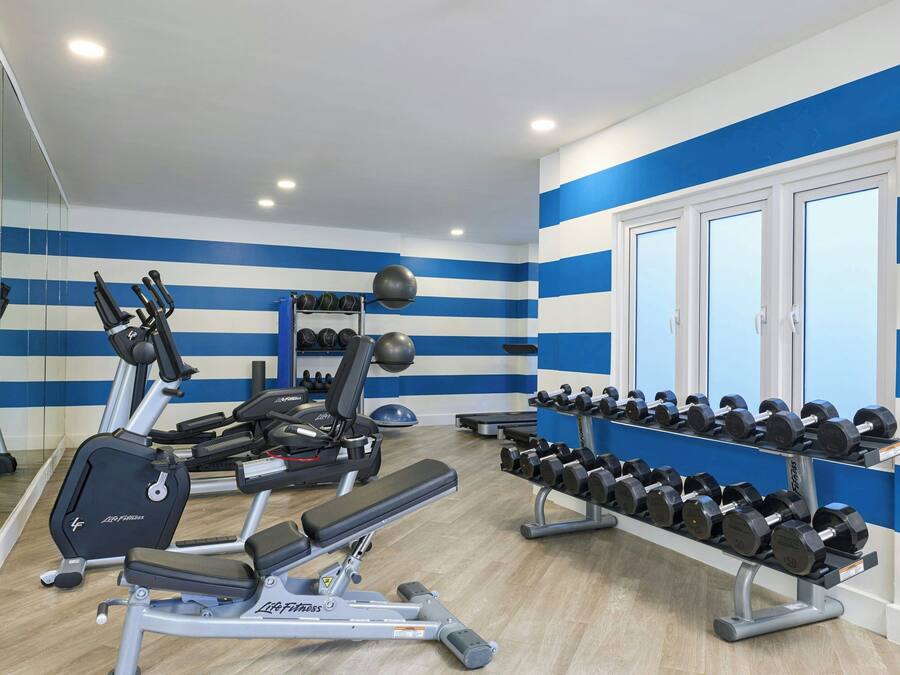 Un gimnasio con equipo de ejercicio, estantes para pesas y un espejo grande.