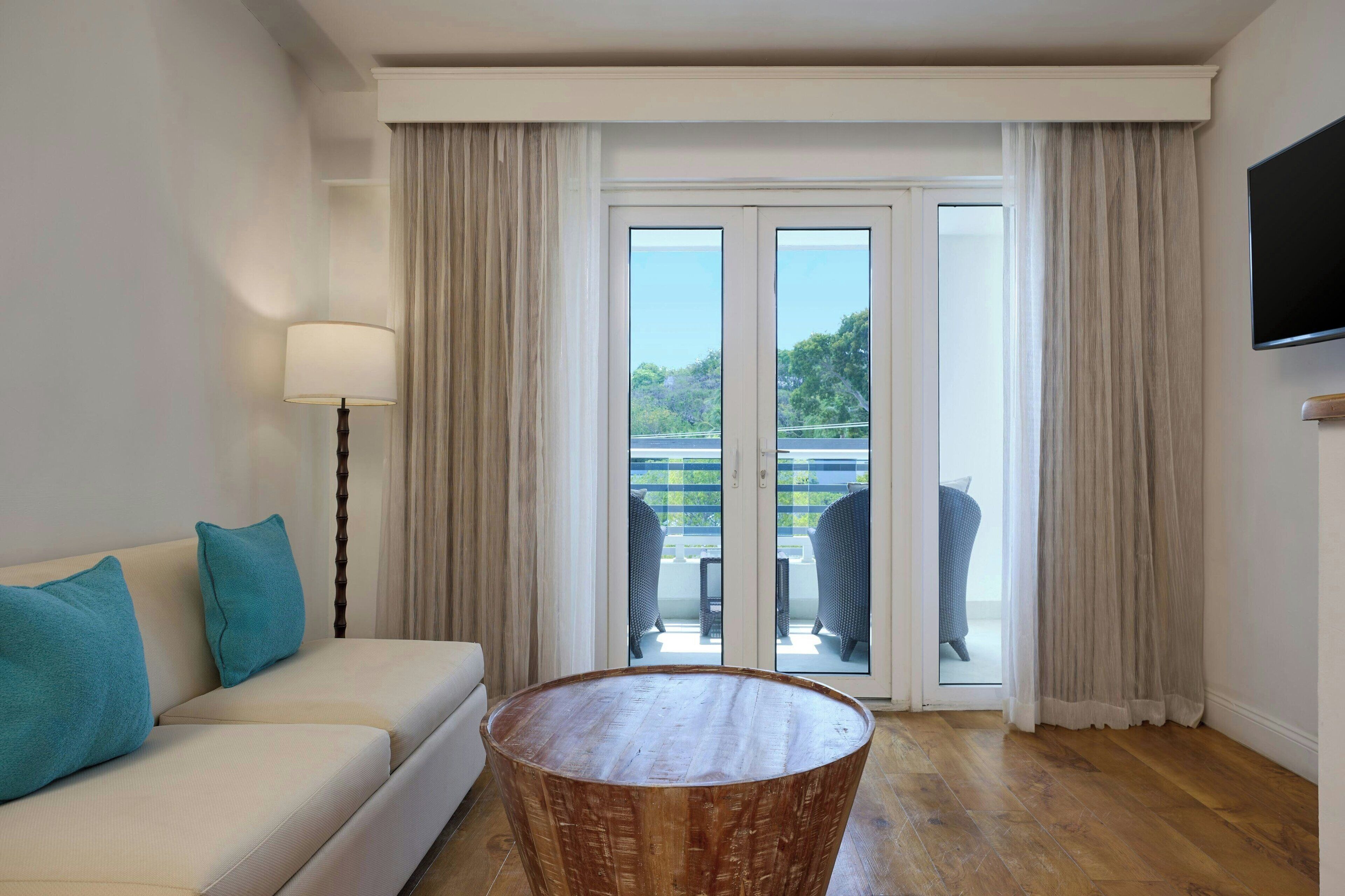 Ein Hotelzimmer mit einer Couch, einem runden Holztisch und einer Glastür, die zu einem Außenbereich mit Stühlen führt.