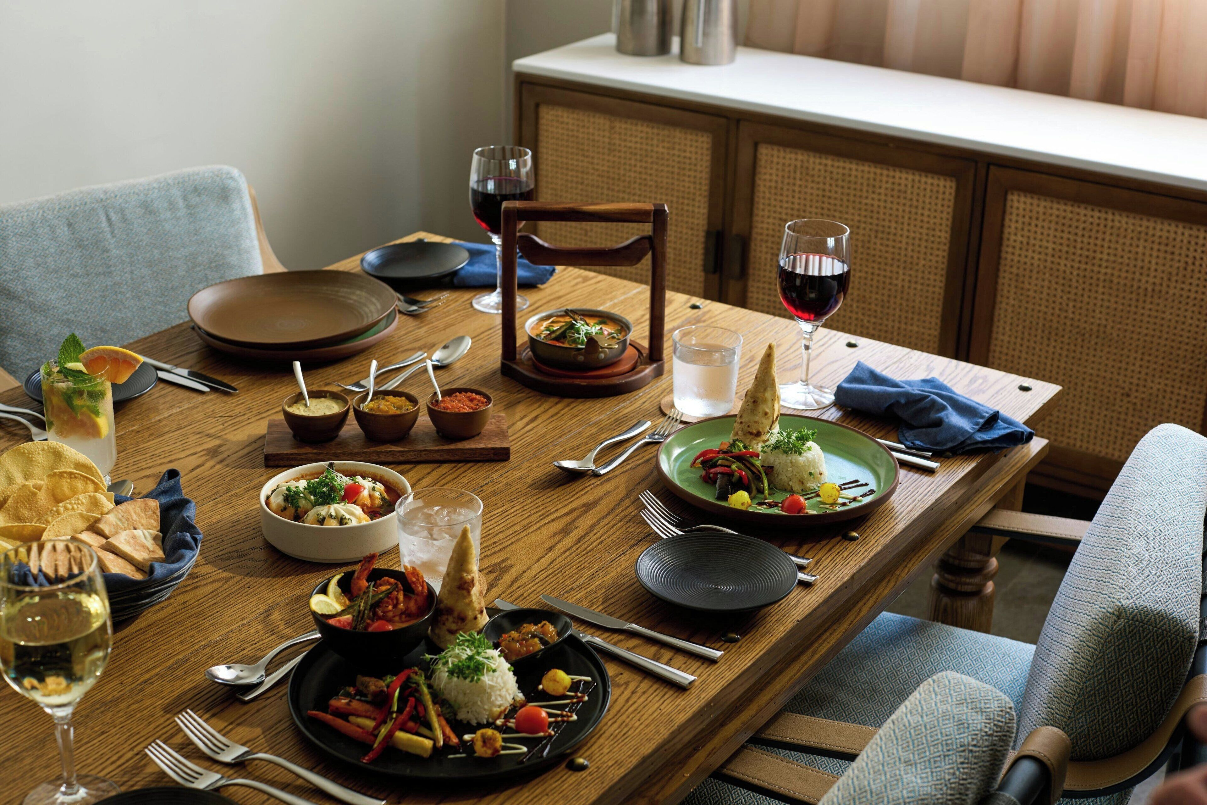 Una mesa de comedor de madera dispuesta con varios platos, copas de vino y cubiertos.