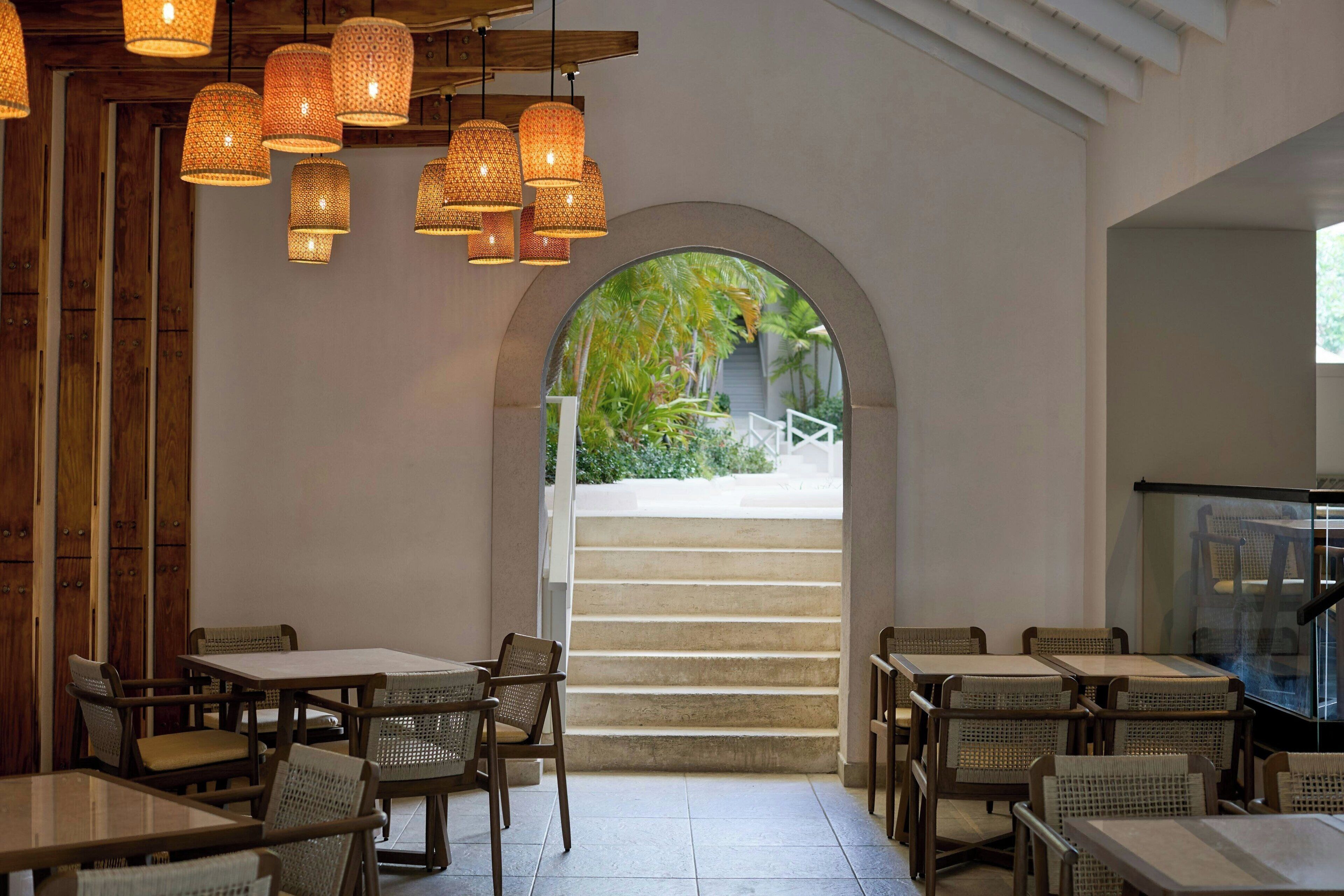 A restaurant with wicker furniture, hanging lights, and a view of a staircase leading outside.