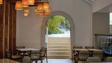 A restaurant with wicker furniture, hanging lights, and a view of a staircase leading outside.