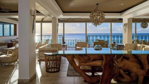 A spacious living area with a glass-top coffee table, wicker chairs, and a view of the ocean. - Waves Resort & Spa, Barbados, An Autograph Collection® All-Inclusive Resort (Prospect)