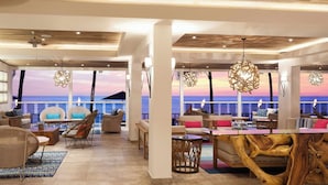 A spacious lounge area with a large wooden coffee table, comfortable seating, and a view of the ocean. - Waves Resort & Spa, Barbados, An Autograph Collection® All-Inclusive Resort (Prospect)