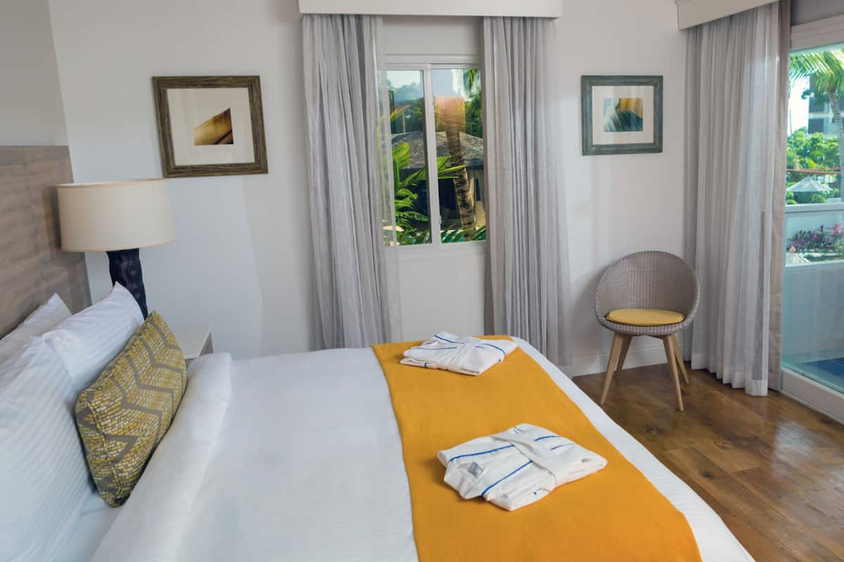Habitación de hotel con cama, una silla, ventana con cortinas y obras de arte en las paredes.