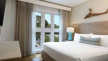 A hotel room with a large bed, a nightstand with a lamp, a wooden headboard, and a view of greenery through the window.