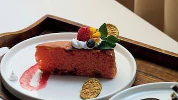 Una porción de pastel de queso en un plato blanco con cobertura de frutos rojos, acompañada de un tenedor y un recipiente pequeño de crema batida.