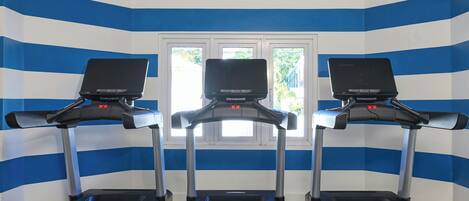 Three treadmills in a room with blue and white striped walls and a window.
