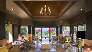 A spacious lobby with a chandelier, comfortable seating, and large windows offering a view of palm trees.