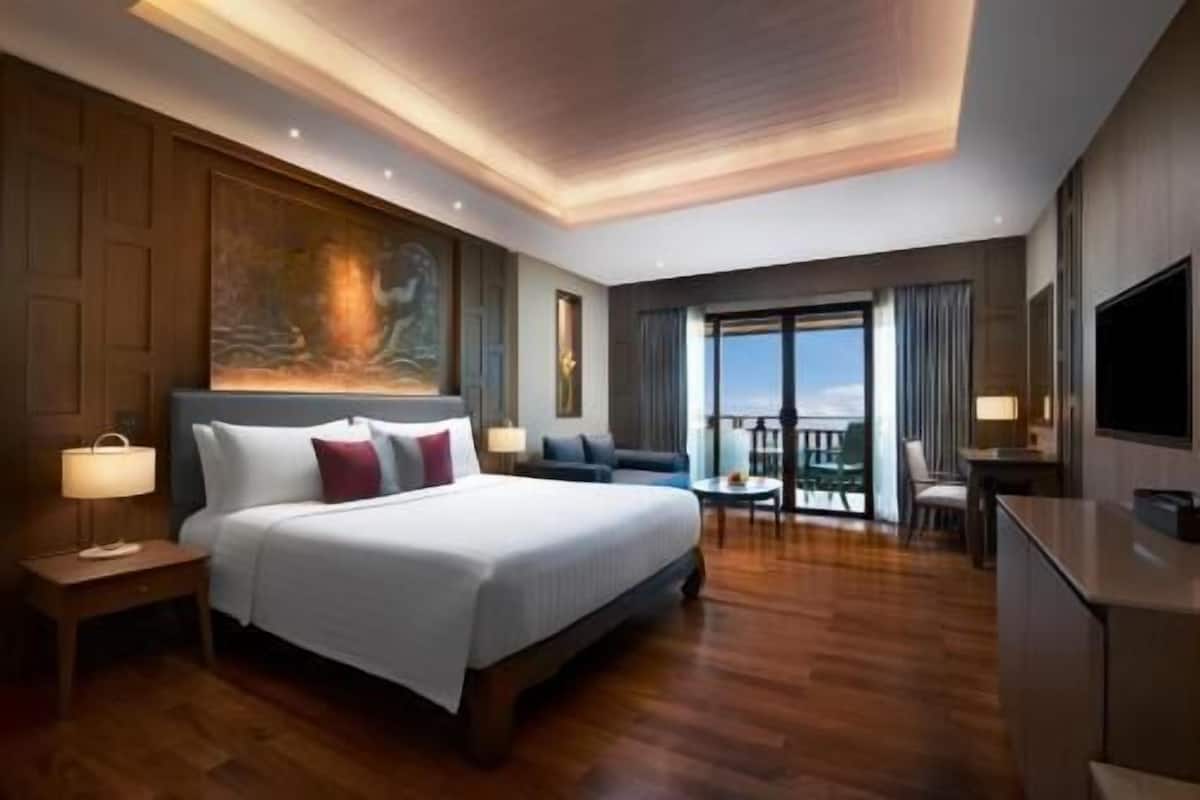 Een hotelkamer met een groot bed, een bureau, een stoel, een televisie en een balkon met uitzicht.