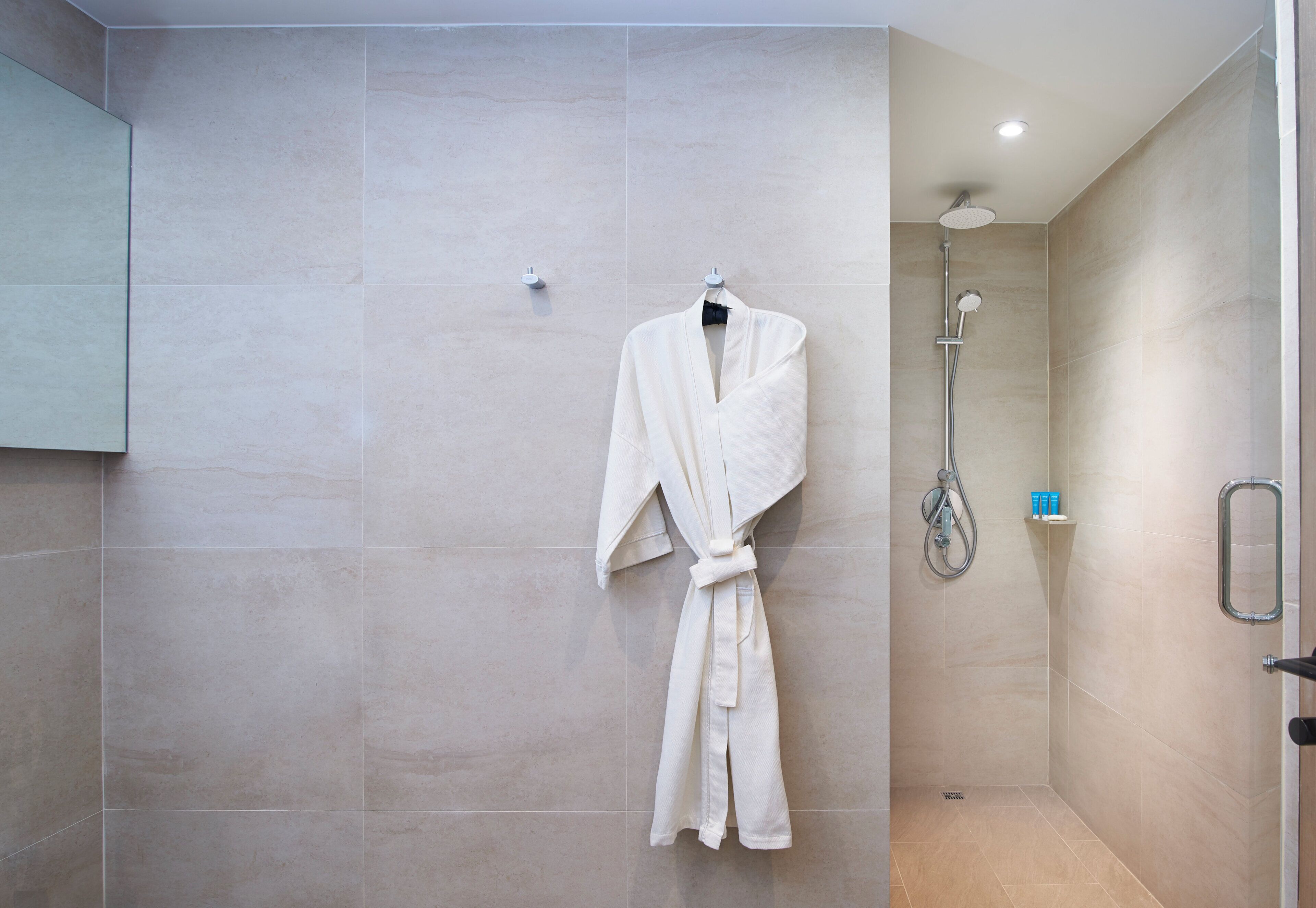 A modern bathroom with a walk-in shower, a robe hanging on the wall, and a small shelf with toiletries.