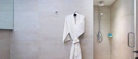 A modern bathroom with a walk-in shower, a robe hanging on the wall, and a small shelf with toiletries.