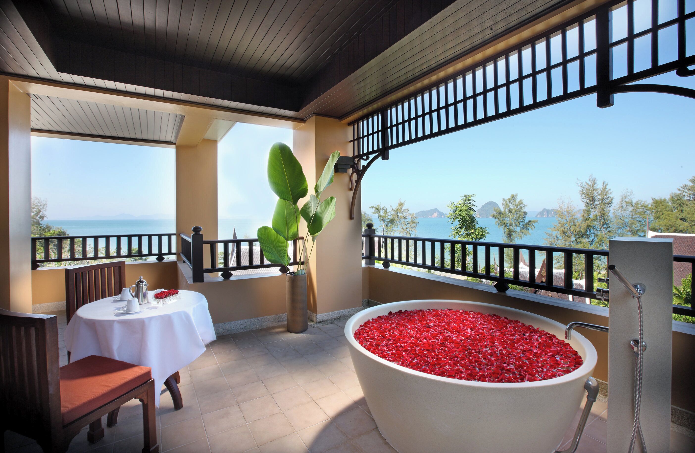 Un balcon avec une table dressée pour le dîner, une grande baignoire remplie de galets rouges et une vue sur la mer.