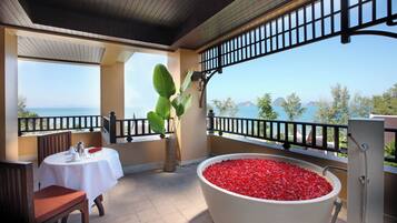 Un balcon avec une table dressée pour le dîner, une grande baignoire remplie de galets rouges et une vue sur la mer.