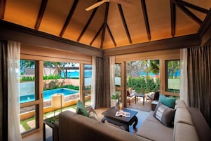 Ampla sala de estar com vista para a piscina, grandes janelas e teto com vigas de madeira.