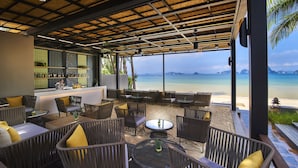 Un espacio de estar al aire libre cubierto con mobiliario de mimbre y vistas a la playa.
