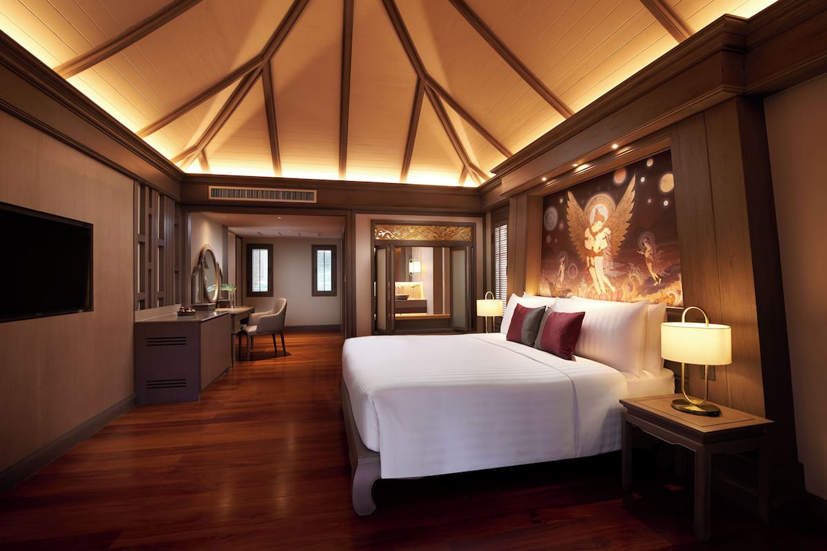 Hotelkamer met een groot bed, nachtkastje met lamp, bureau met stoel, kaptafel met spiegel en een decoratieve muurdecoratie.