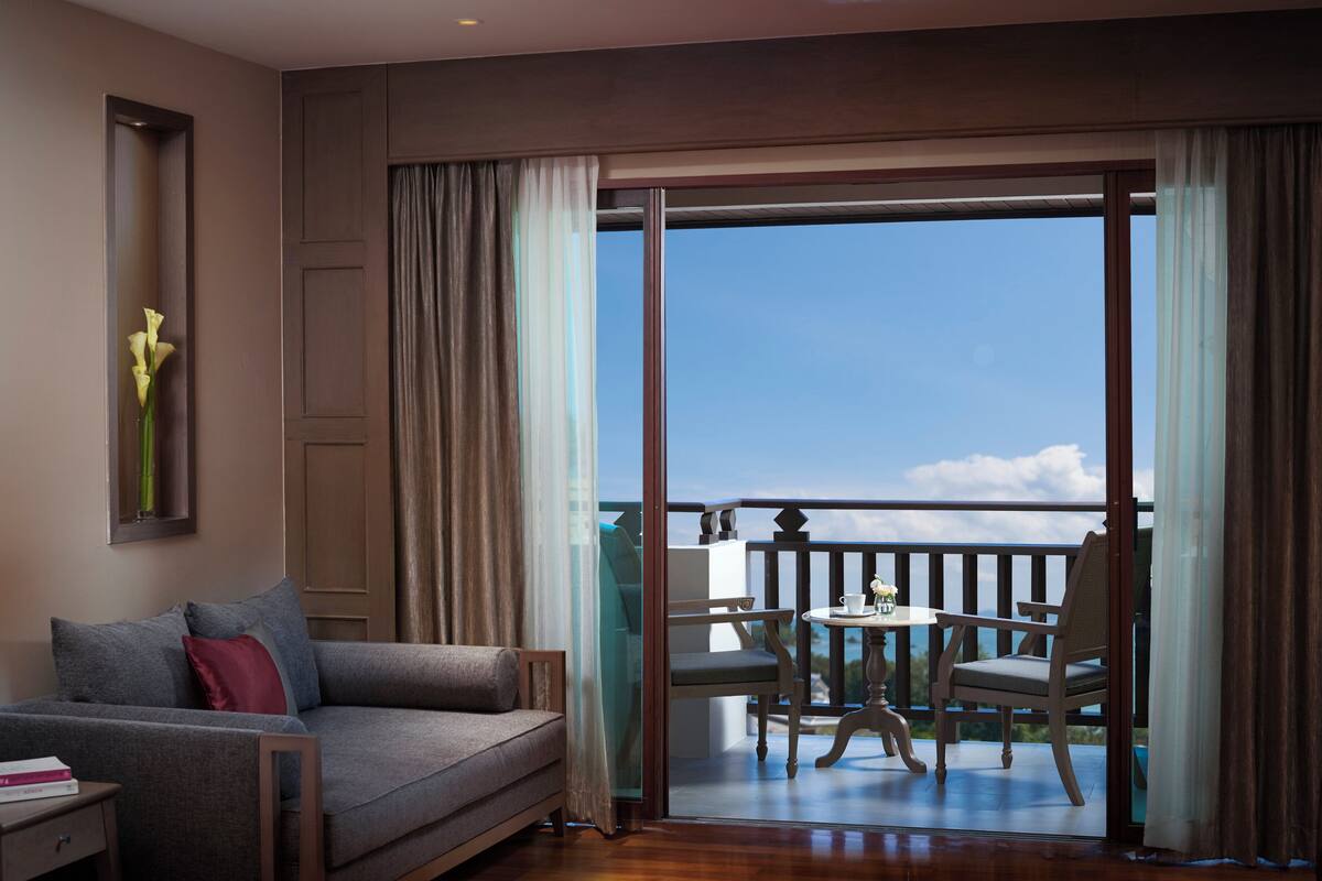 Een hotelkamer met een bank, een kleintje tafeltje en een balkon met een tafel en stoelen.
