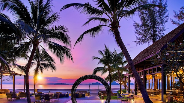 Un resort con asientos al aire libre, un elemento decorativo circular y vista al océano al atardecer.