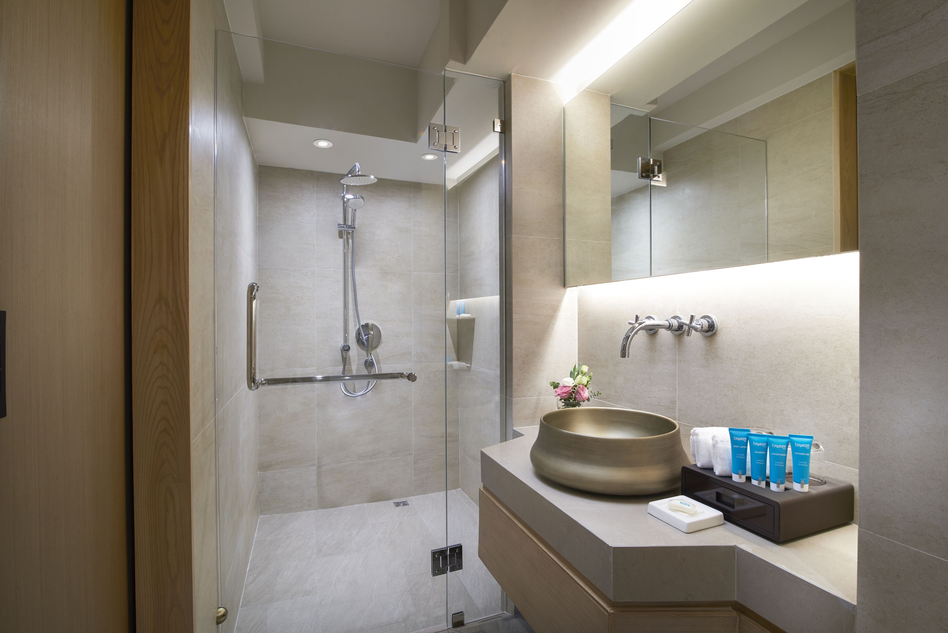 A modern bathroom with a glass-enclosed shower, a large mirror, and a vanity with toiletries.