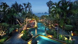 Un área de piscina en un complejo turístico, con varias piscinas, sillas de descanso y exuberante vegetación tropical.