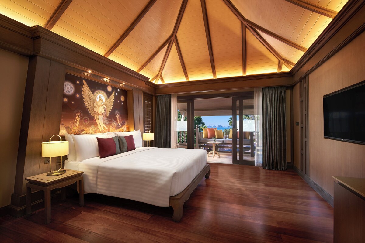 Une chambre d’hôtel spacieuse, dotée d’un grand lit, d’une table de chevet avec une lampe, d’une télévision et offrant une vue sur l’extérieur grâce à une porte-fenêtre coulissante.