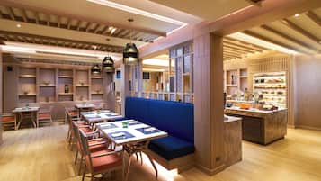 Un interior de restaurante moderno con mobiliario de madera, asientos acolchados azules y una vitrina con postres.