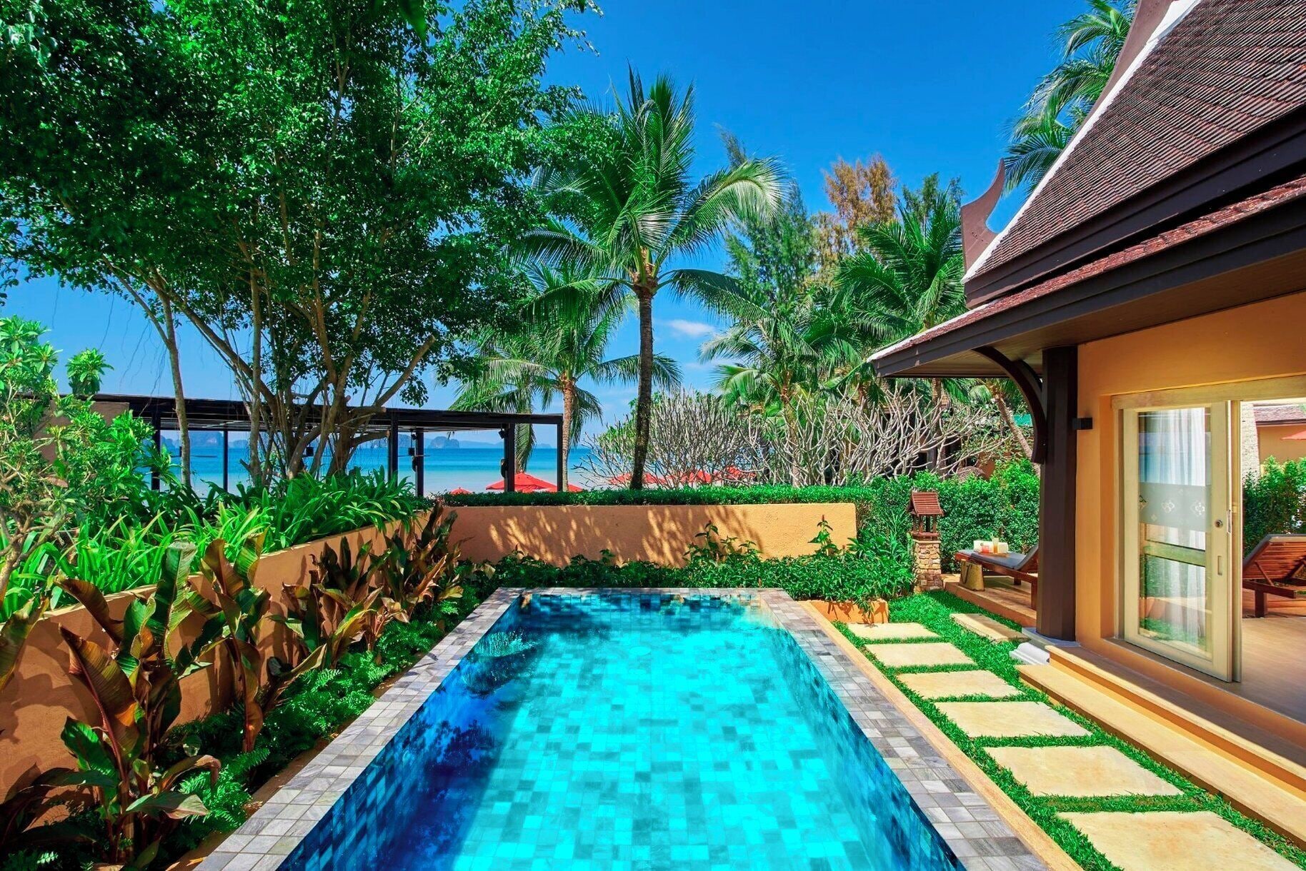 A swimming pool with a view of the ocean, surrounded by lush greenery and palm trees.