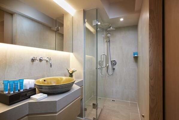 A modern bathroom with a glass-enclosed shower, a large sink, and toiletries on the counter.