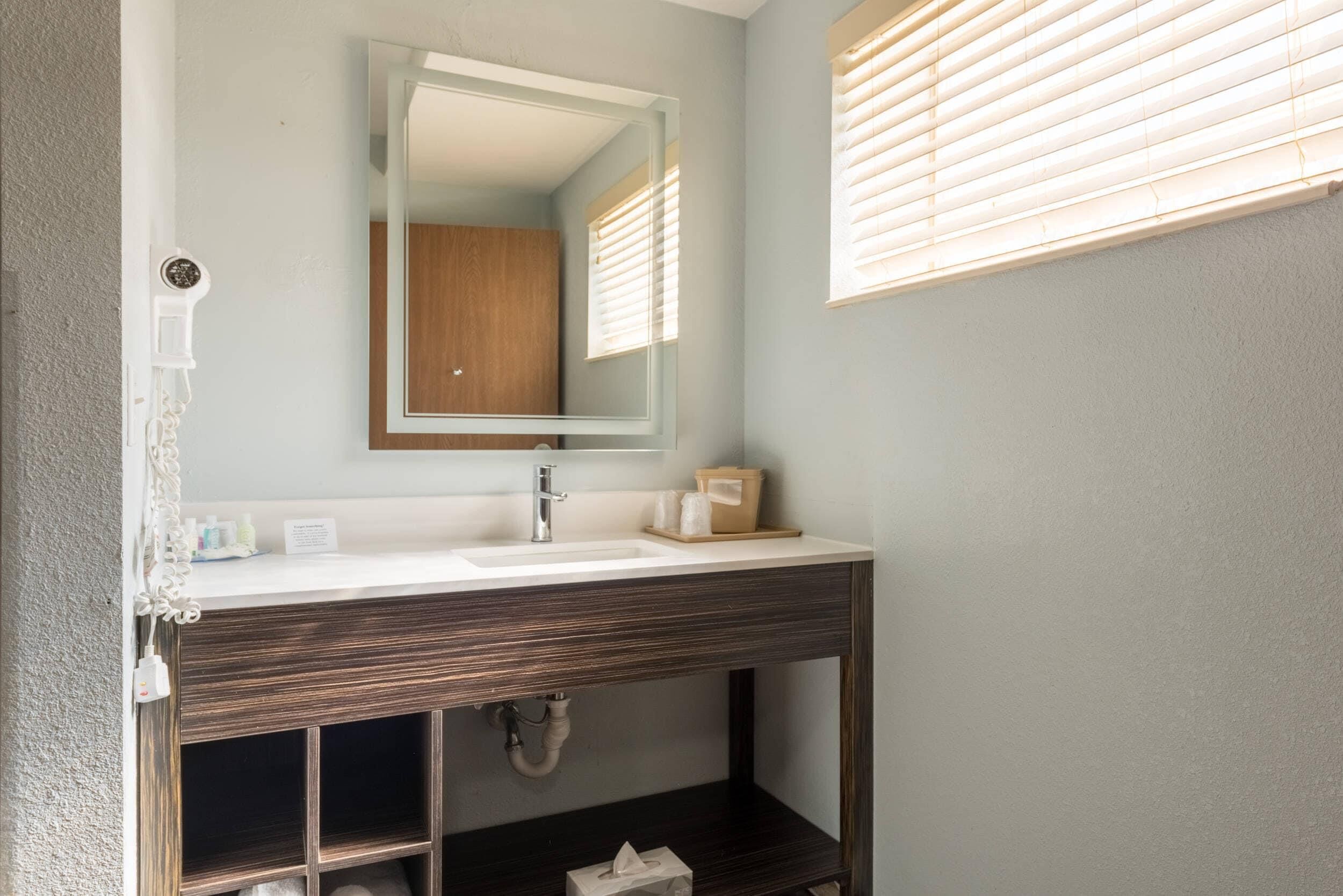 A bathroom with a wooden vanity, a mirror, a sink, and a window with blinds.