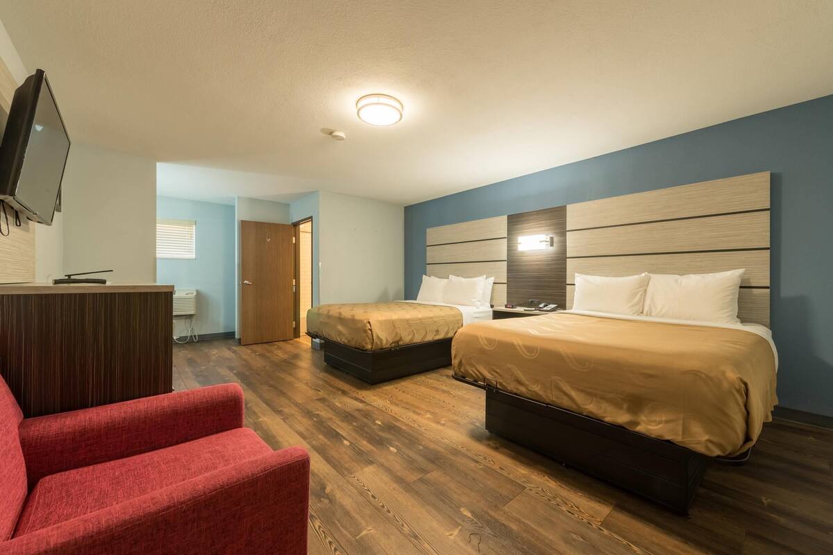 Una habitación de hotel con dos camas, televisión, escritorio y una silla roja.