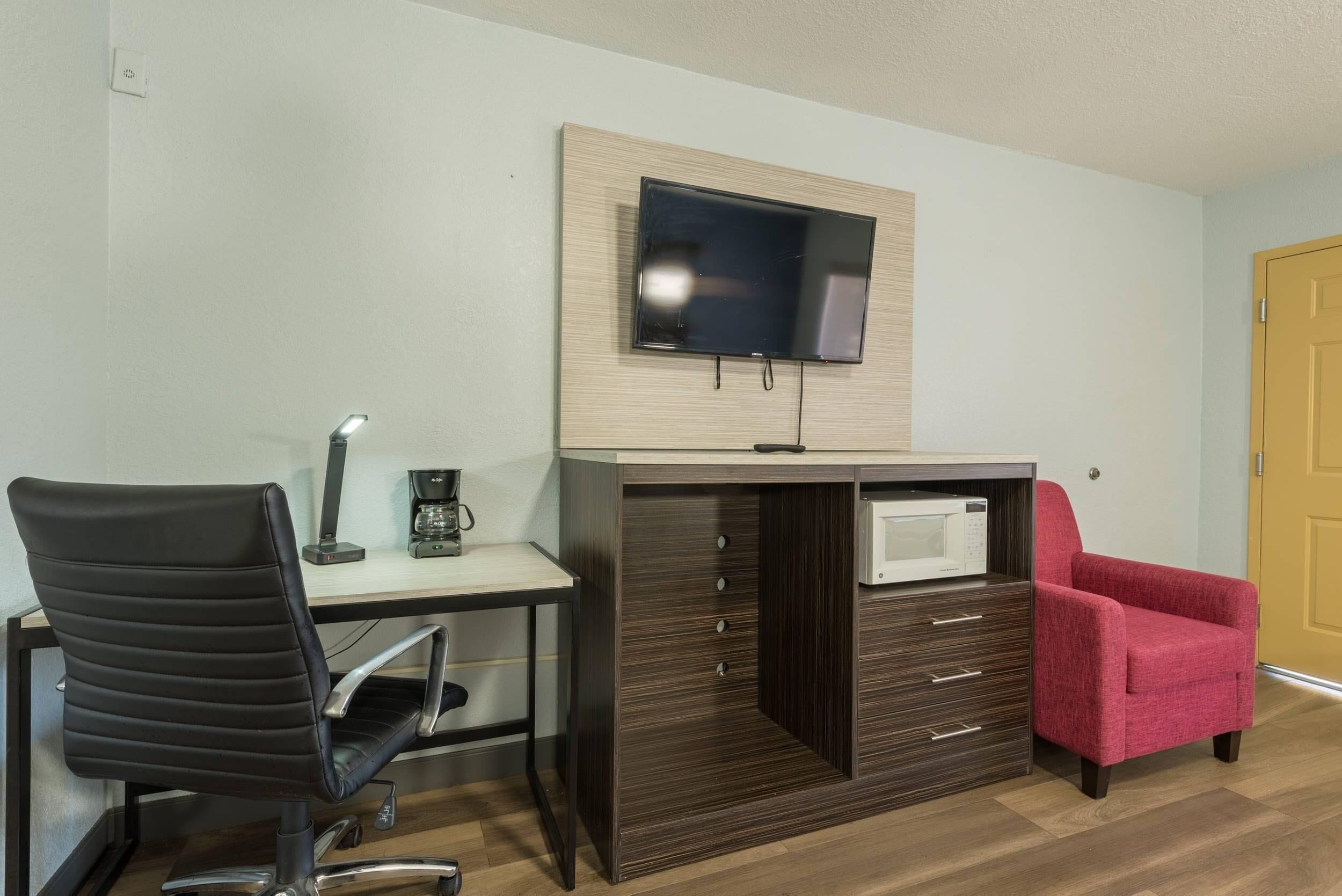 Quarto com escrivaninha, cadeira, TV fixada na parede e gaveta com micro-ondas.