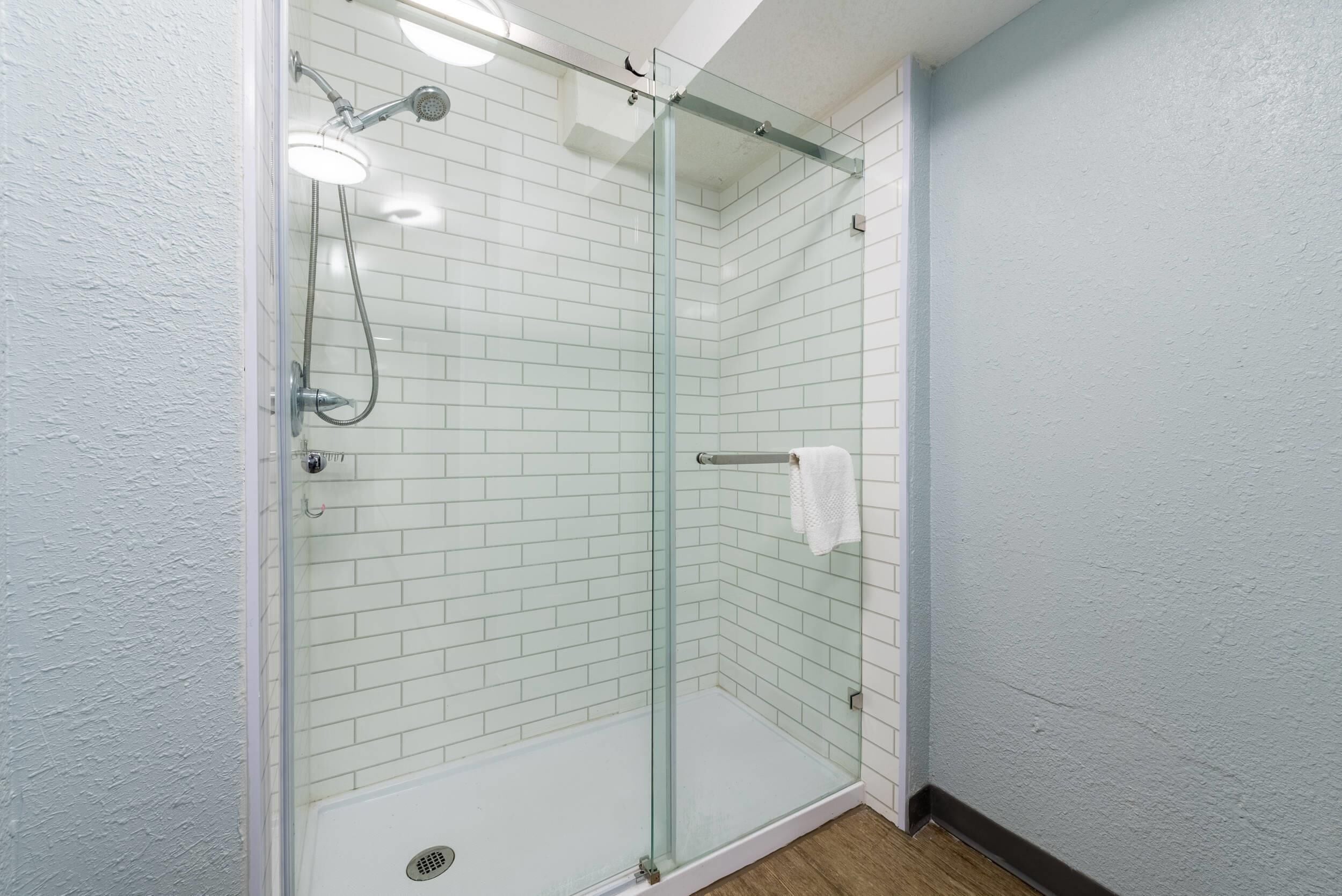 A glass-enclosed shower with white tiled walls and a wooden floor.