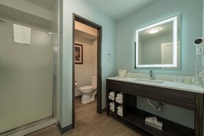 A bathroom with a shower, toilet, vanity with a mirror, and towel storage.