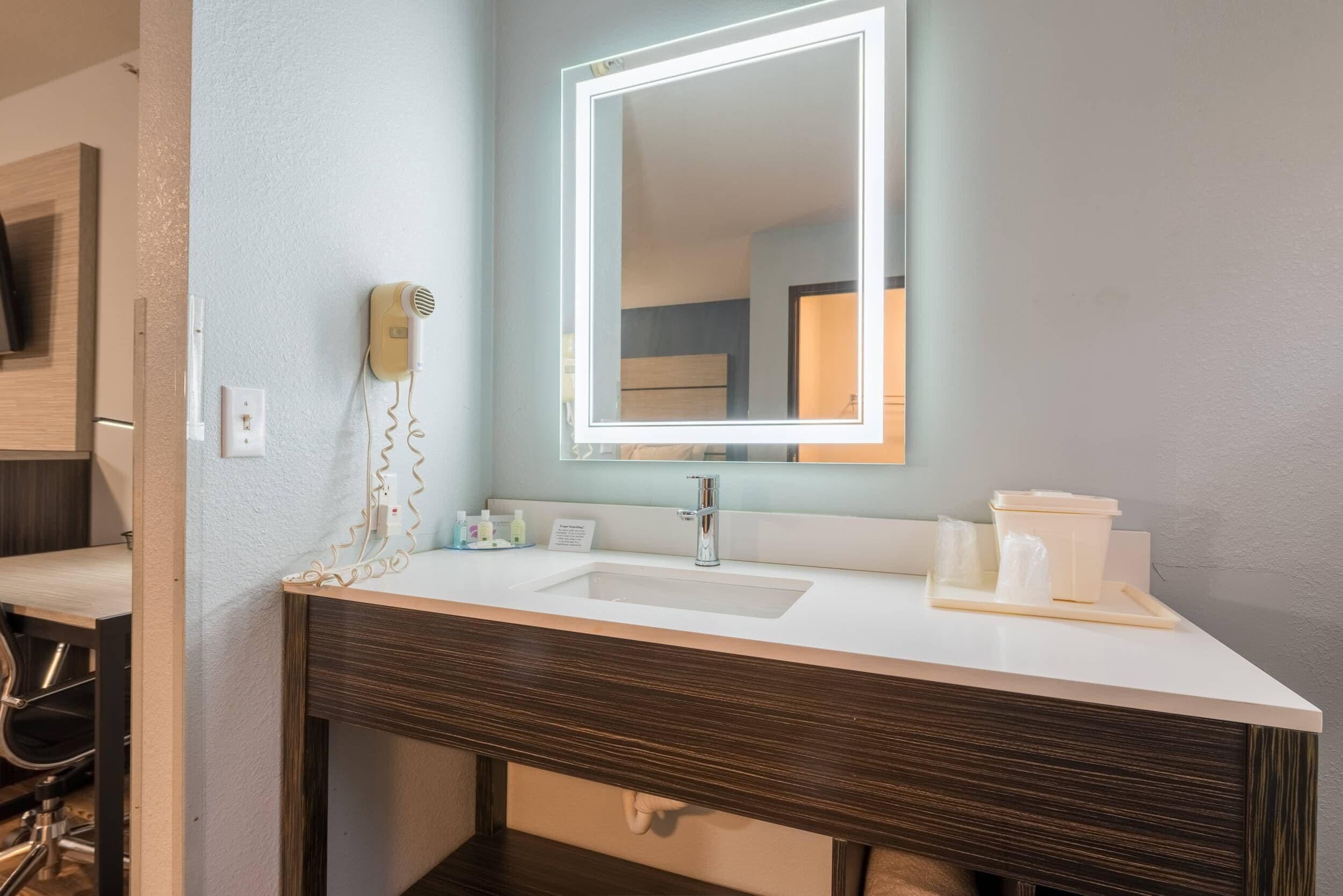 Une salle de bain moderne avec un lavabo blanc, un grand miroir et un sèche-cheveux fixé au mur.