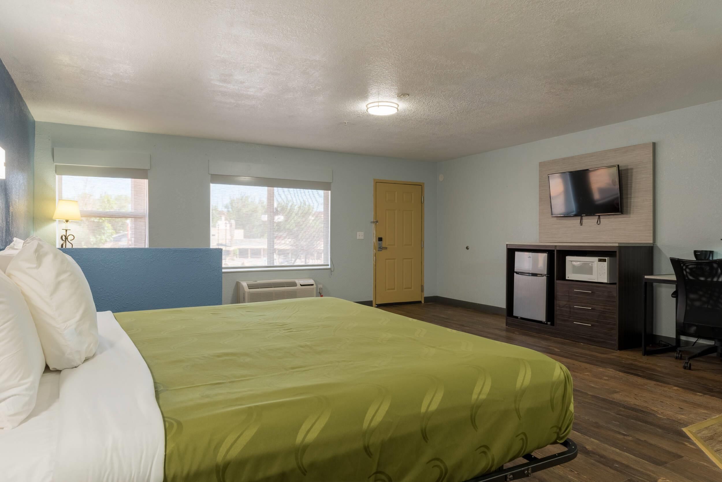 Een hotelkamer met een bed, bureau, televisie en raam.
