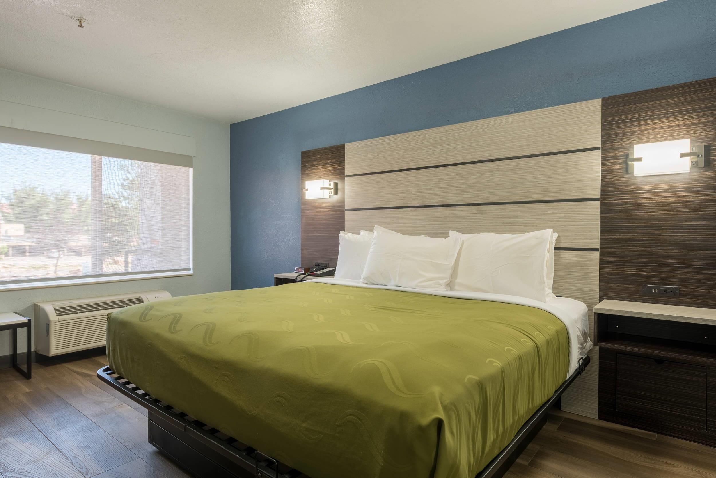 A hotel room with a bed, bedside tables, a window, and a wall-mounted light fixture.