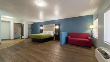 Quarto de hotel com uma cama, um sofá vermelho, uma mesa de cabeceira, um abajur e um ar condicionado.