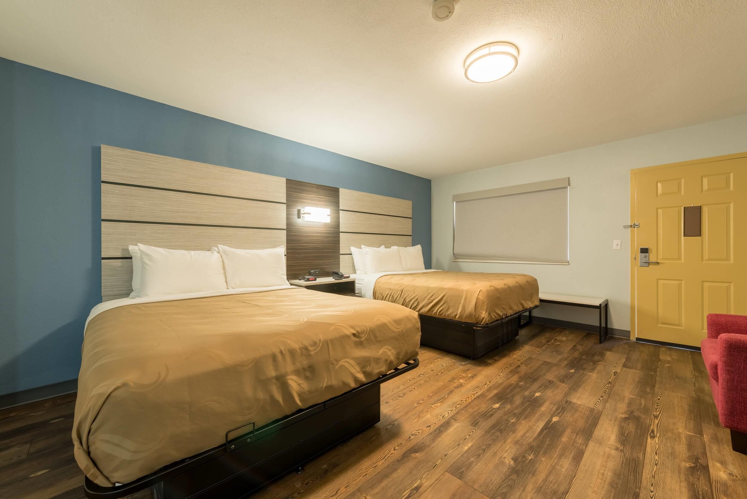 A hotel room with two beds, a wooden floor, a blue wall, and a yellow door.