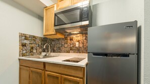 A compact kitchen with wooden cabinets, a stainless steel refrigerator, a microwave, and a stone-patterned backsplash. - Quality Inn & Suites Manitou Springs at Pikes Peak / Garden of the Gods (Manitou Springs)