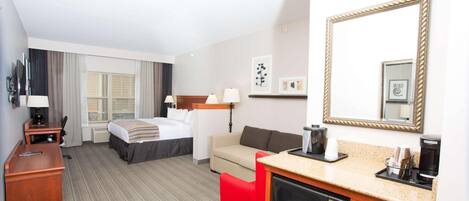 Una habitación de hotel con cama, escritorio, sofá, máquina de café y microondas.