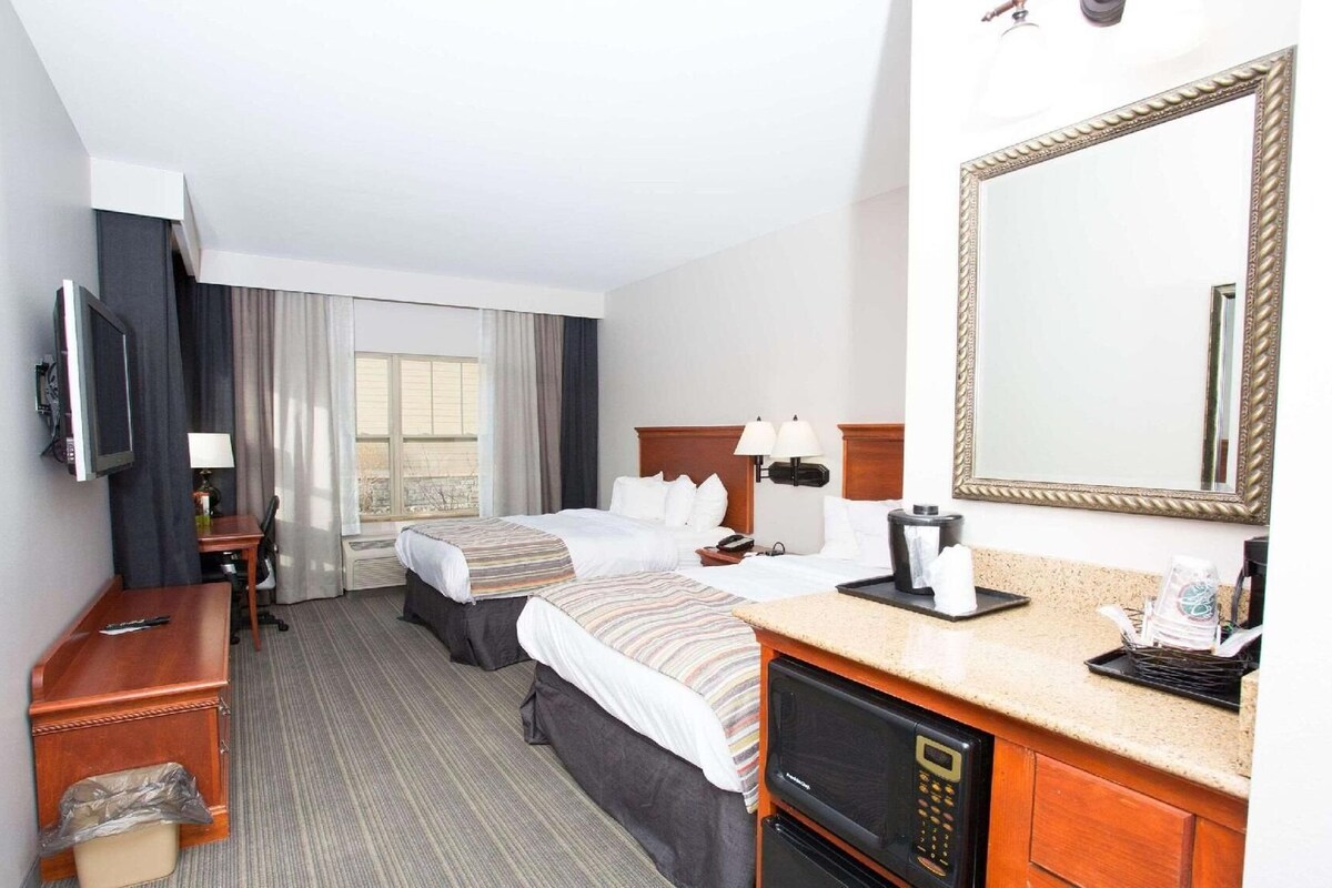 Une chambre d’hôtel équipée d’un lit, de tables de chevet, d’une télévision, d’un four à micro-ondes et d’un grand miroir.