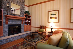 A cozy living room with a fireplace, comfortable seating, and a bookshelf. - Country Inn & Suites by Radisson, Grand Forks, ND (Grand Forks)