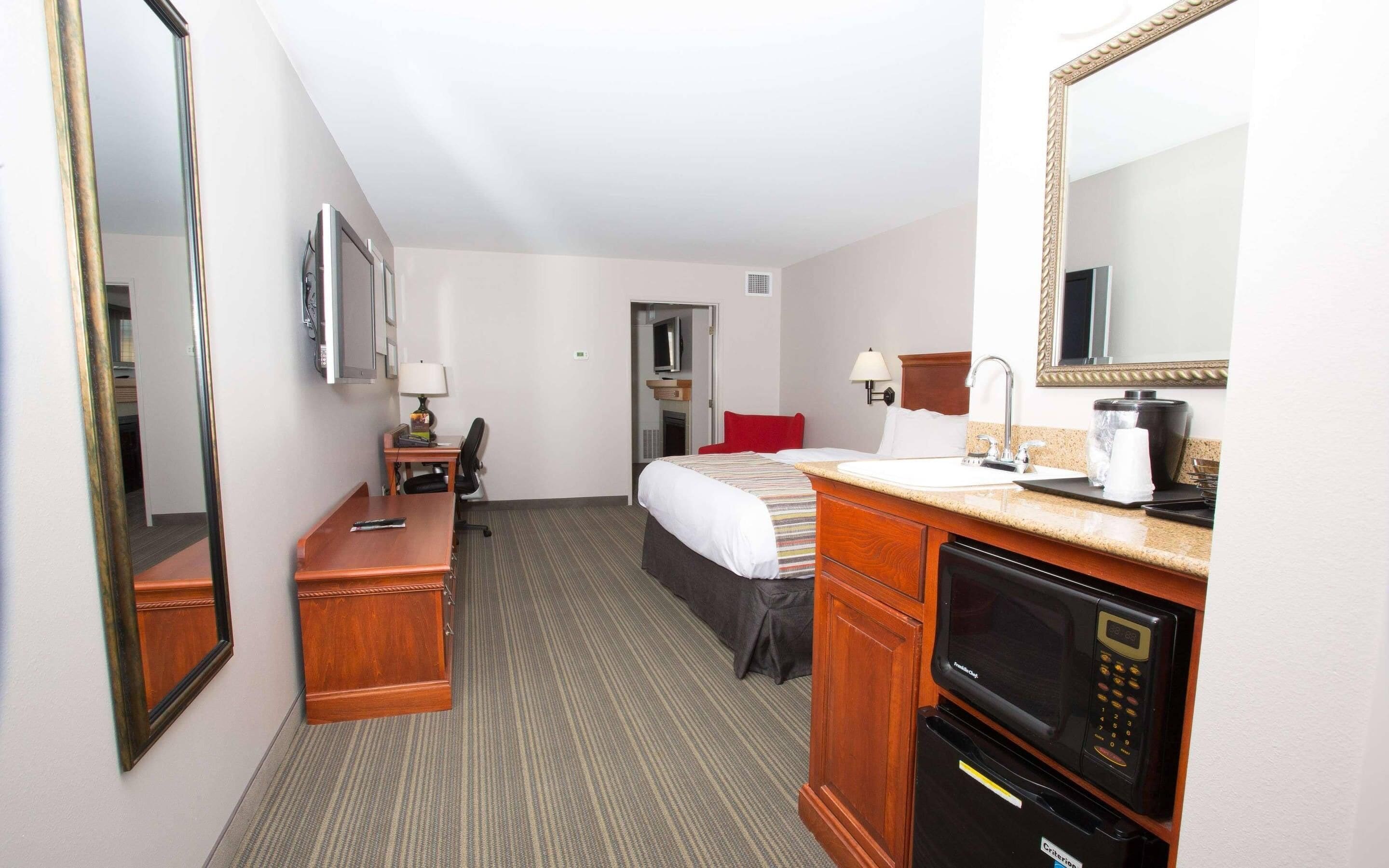 Een hotelkamer met een bed, een bureau, een stoel, een bureaulamp, een koffiezetapparaat, een magnetron en een koelkast.